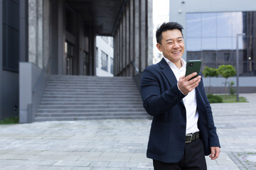 Portrait of Asian cheerful and successful businessman near office in business suit got good news read good news online