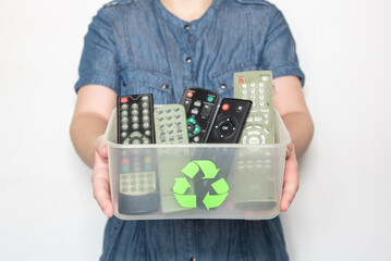 Mujer sosteniendo una caja de plástico transparente con el símbolo del reciclaje, llena de controles remotos y mandos a distancia de televisión viejos - obrazy, fototapety, plakaty
