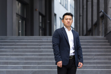 Portrait of asian serious businessman near office in business suit confident broker sales manager