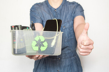 Mujer sosteniendo una caja de plástico transparente con el símbolo de reciclaje, llena de mandos...