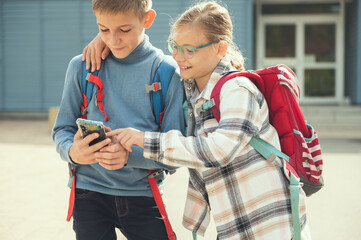 Happy school children playing and making selfies with cellphone at schoolyard after lessons