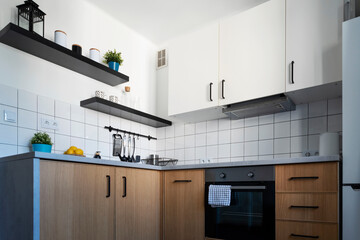 Modern kitchen with wooden cabinets and white tiles and utensils. Kitchen counter in cozy interior for cooking.
