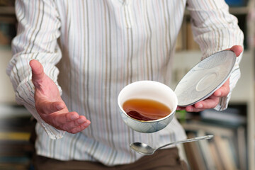 A man in sripy shirt dropping teacup with tea, selective focus