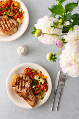 Delicious hearty dinner in plates on the table and a bouquet of beautiful autumn flowers, fried pork entrecote on the bone with stewed vegetables and fresh salad with mozzarella