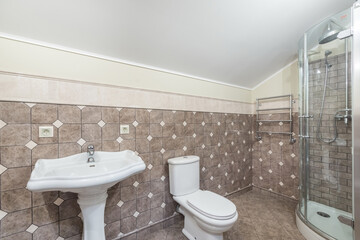 The bathroom is decorated with brown and white tiles. The shower cabin is equipped with a tropical watering can. Interior of a cottage or townhouse
