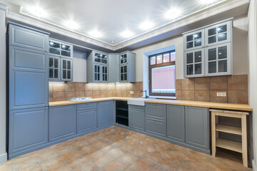 Stylish kitchen with a window, the facade of the set is made in blue color. The floor is covered with brown granite tiles. Interior of a cottage or townhouse