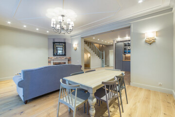 Modern design of the living room in blue tones with a fireplace, a sofa and a dining table with chairs. Interior of a cottage or townhouse