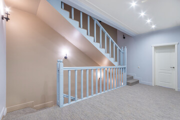 A spacious entrance hall with stairs leading to different floors. The interior is decorated in pastel colors. Interior of a cottage or townhouse