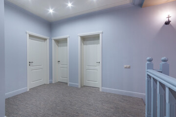 A spacious corridor in blue color with three white doors and a floor covered with gray carpet. Interior of a cottage or townhouse