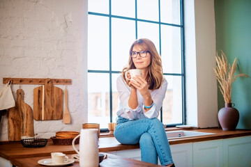 Smiling mature woman drinking her morning coffee in the kitchen at home