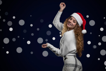 Latino woman wearing Christmas hat and clothes pointing to a space for text, with out-of-focus lights in the background
