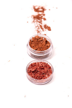 Creative photo of cosmetic swatches. Broken eye shadows in bronze colour and make up brush on a white background 