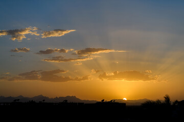 Dramatic sky over silhouettes of trees and mountain at sunset