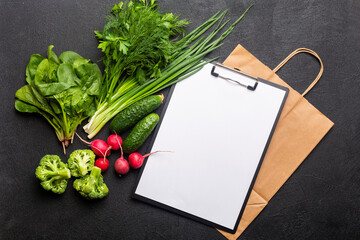 Concept: Purchase healthy clean food for vegetarians: vegetables, nuts and legumes top view on a black background with a paper bag and a white notebook for a list of products.