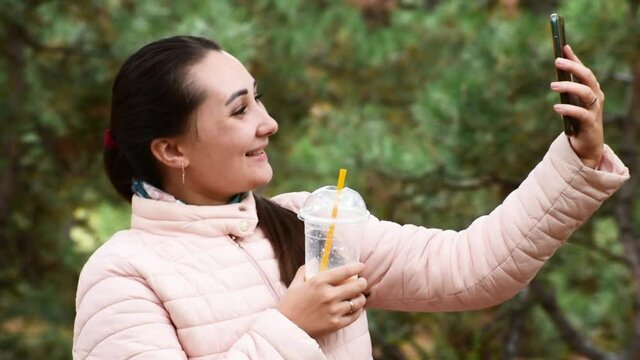 Pretty Girl makes selfie or speaking with video on telephone in the park. Autumn background. 