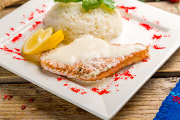 salmon steak in cream sauce with rice on wooden table close up