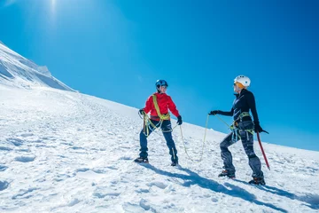 Crédence de cuisine en verre imprimé Mont Blanc Two laughing to each other young women Rope team ascending Mont blanc du Tacul summit 4248m dressed mountaineering clothes with ice axes on snowy slopes. People extreme activities sporty concept image