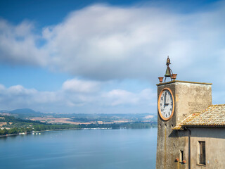 Moving clouds above lake Bolsena and medieval tower with clock with copy space