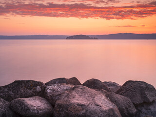 Fototapeta na wymiar beautiful sunrise on lake Bolsena with view to island and gian stones on foreground with copy space