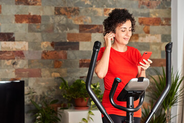 Fototapeta na wymiar Woman exercising at home on cross training elliptical using mobile phone