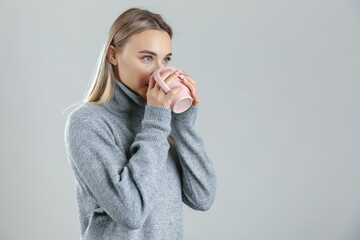 woman wearing warm sweater drinks a hot tea on grey background, studio shot. the concept of warming up with a hot drink. 