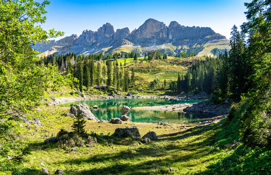 Der berühmte Karersee / Lago di Carezza in den Dolomiten, Südtirol: Panoramabild mit Blüten und Berggipfeln