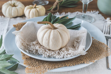Place setting on a wooden table with white mini pumpkins, sage leaves and natural decoration for...