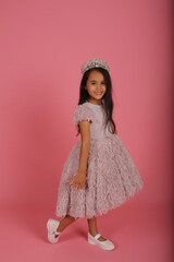 a small dark-skinned beautiful girl in a lush pink dress with a crown on her head
