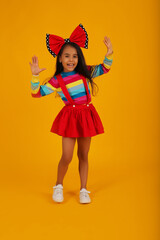 a dark-skinned happy girl in a red skirt in a colored jacket with a red polka dot bow on her head on a yellow background