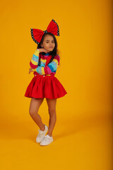 a dark-skinned happy girl in a red skirt in a colored jacket with a red polka dot bow on her head on a yellow background