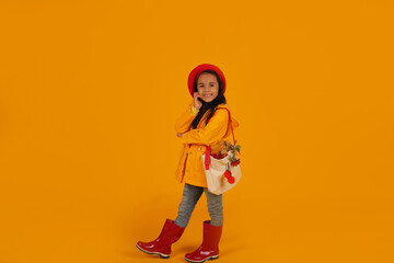 Fototapeta na wymiar a girl in a red beret with pink glasses in a yellow raincoat and red boots has a bag with autumn flowers on her shoulder