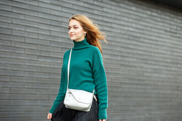 Beautiful adult woman stands near a black wall. Green knitted sweater and black skirt. - Powered by Adobe