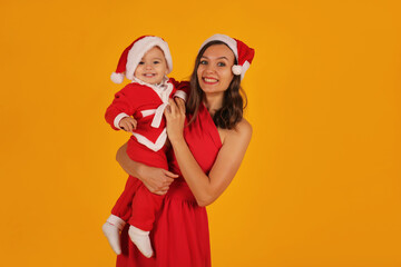 Fototapeta premium a beautiful young girl in a red dress holds her son in a Santa Claus costume and a Santa Claus hat for the new year