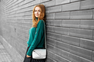 Beautiful adult woman stands near a black wall. Green knitted sweater and black skirt.