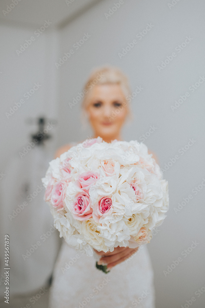 Poster Vertical shot of a glamourous bride holding and showing her bridal bouquet of white roses