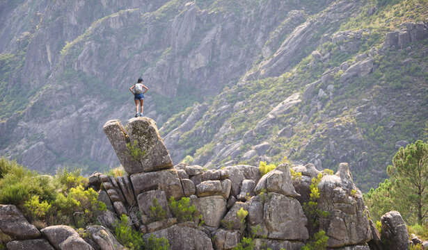 Rapariga no topo de uma pedra no cimo de uma montanha a ver a paisagem, escalada