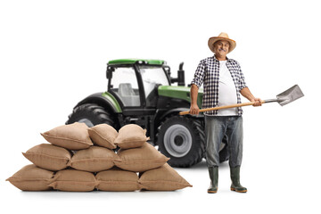 Mature farmer with a straw hat holding a shovel with a tractor in the background