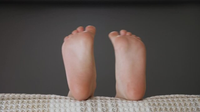 Bedtime child lying in sofa and move of music bare feet close up. Child legs waving in bed having fun barefoot kid moving feet and toes. Pair of legs closeup. Child feet in bed. Little leg playing bed