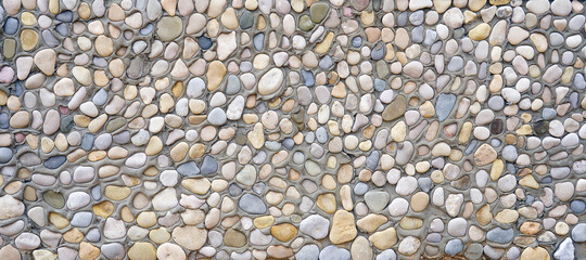 A gray concrete wall made of cement with a lot of sea stones and pebbles of different colors