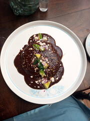 Mole enchiladas with cheese and avocado rolled tortillas stuffed with chicken, typical Mexican dish made at home with chili, chocolate, pepper, cumin, peanut and sesame
