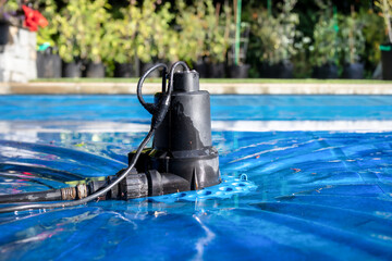 Automatic pool cover pump on top of blue wet cover in front of defocused garden foliage....