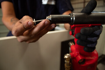 The worker uses a rivet hand gun, and inserts a rivet into it. Manual rivet wrench.