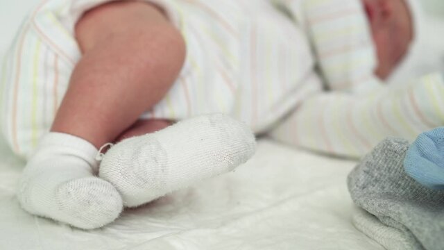 Tiny Cute Newborn Babies Feet In Socks Early First Days Of Life On White Background. Close up of Small Legs of Infirm Baby Infant Sleeping Sweetly on Soft Comfortable Bed. Childhood, Maternity Concept