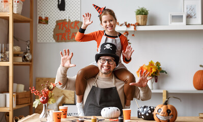 Little girl sitting on father shoulders making scary gesture while making Halloween home decorations