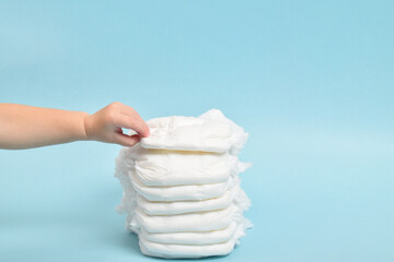 A child's hand takes a diaper-panties on a blue background. Pesto for the text. a place to copy.