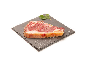 chuletón de buey fresco crudo con hojas de laurel seco y sal gorda decorativa sobre un plato de pizarra negro.  aislada fondo blanco