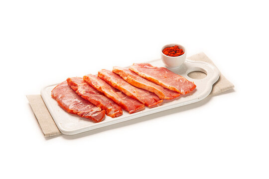 lomo de cerdo adobado fresco cortado en filetes sobre bandeja blanca con pimenton en bol blanco decorativo, sobre servilleta de tela marron. aislada fondo blanco