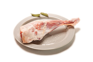 pierna de cordero lechal crudo fresco en plato gris con hojas de laurel seco y sal gorda decorativo. aislada fondo blanco