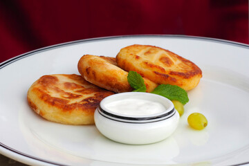 Round curd cheesecake, curd fritters. Sweet fried cheese pancakes on white plate, mint and sour cream. Home tea party
