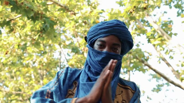 Man in traditional blue Tuareg dresses, danced in a park. Blurred background of trees.